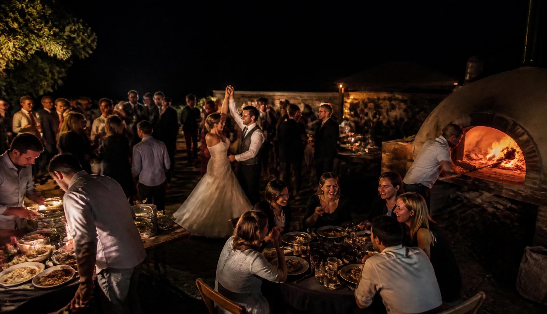 Horno de leña encendido durante la fiesta de una boda de noche, con invitados alrededor