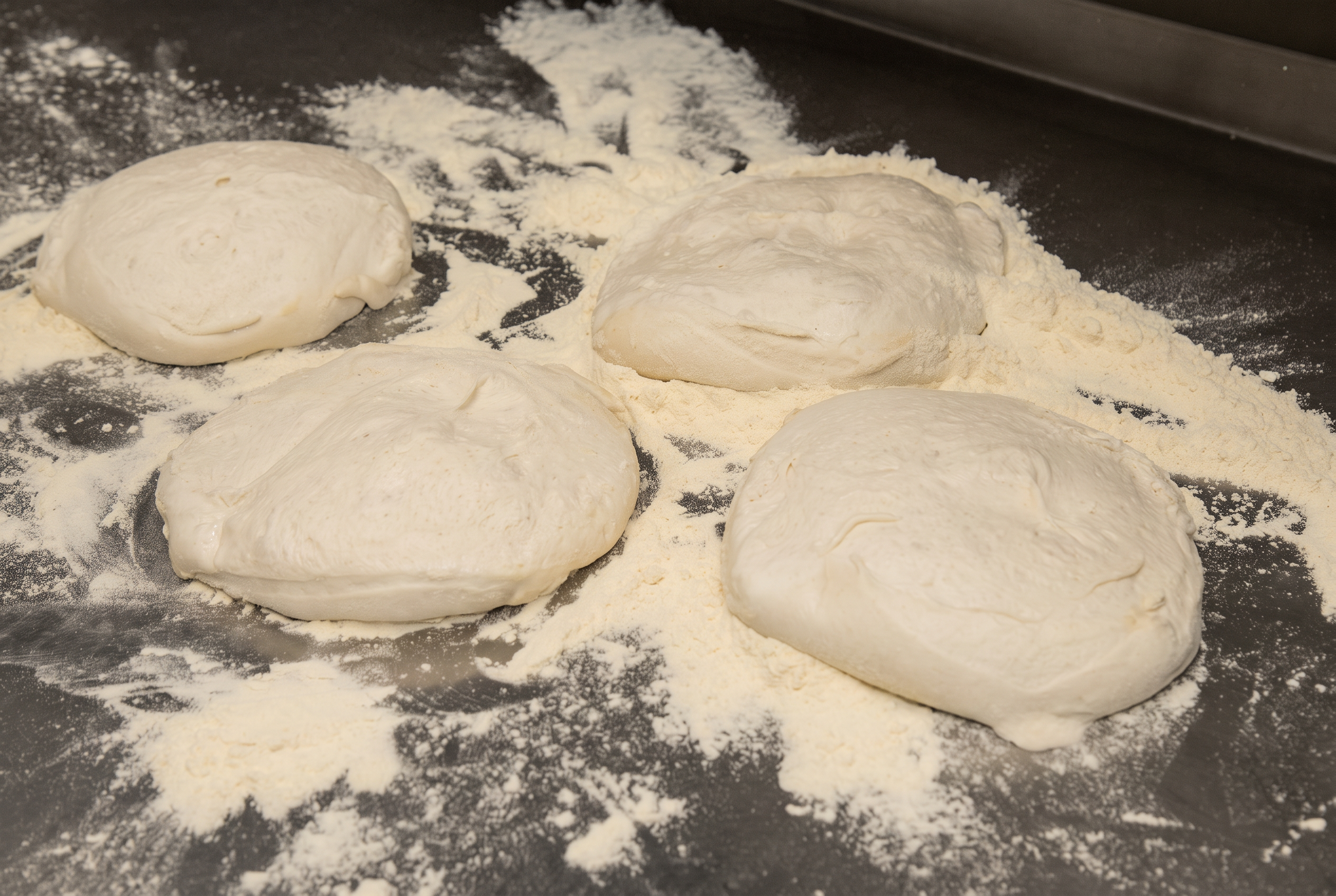 Cuatro porciones de masa de pizza Chifla reposando sobre harina