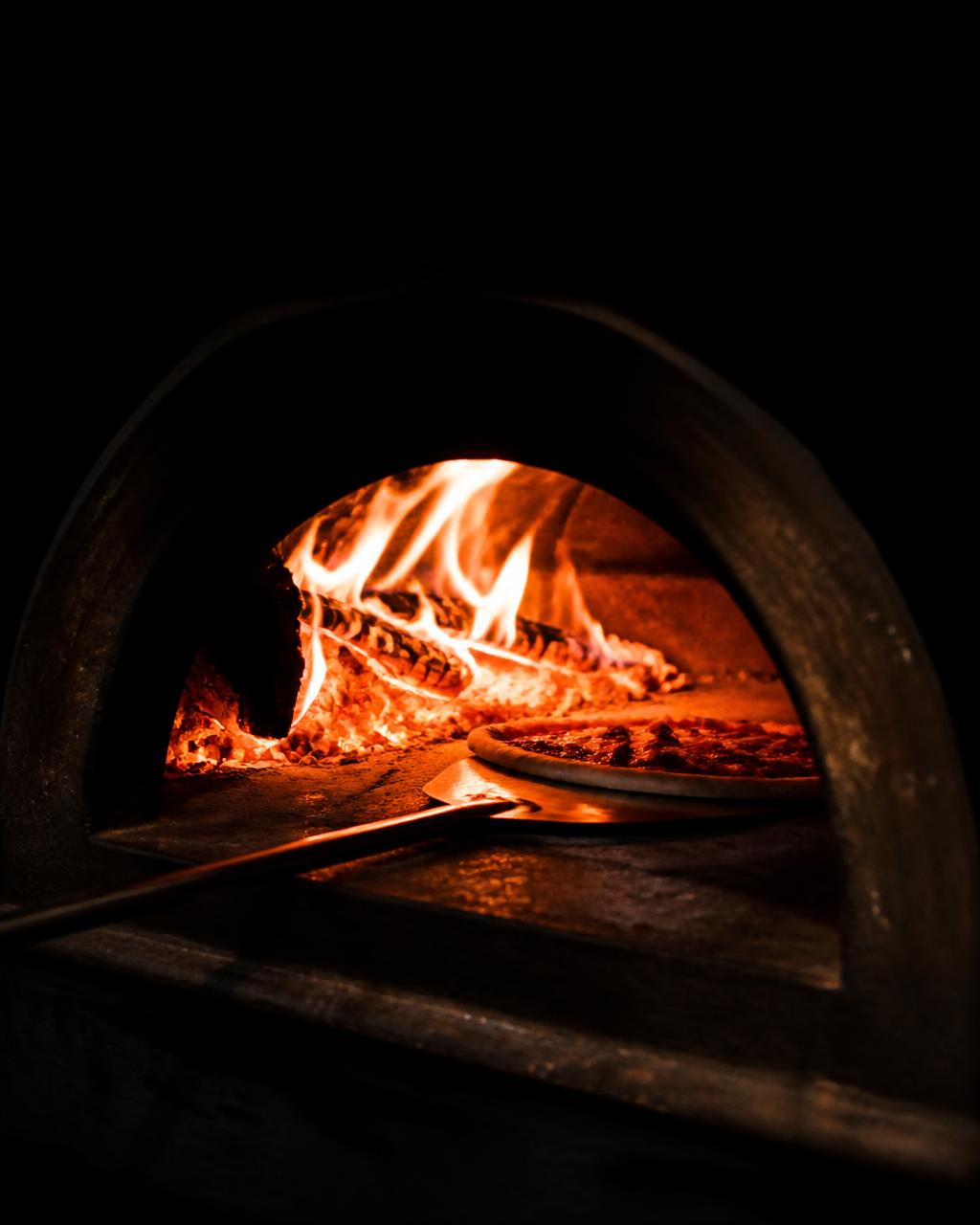 Pizza dentro del horno de leña con las llamas al fondo